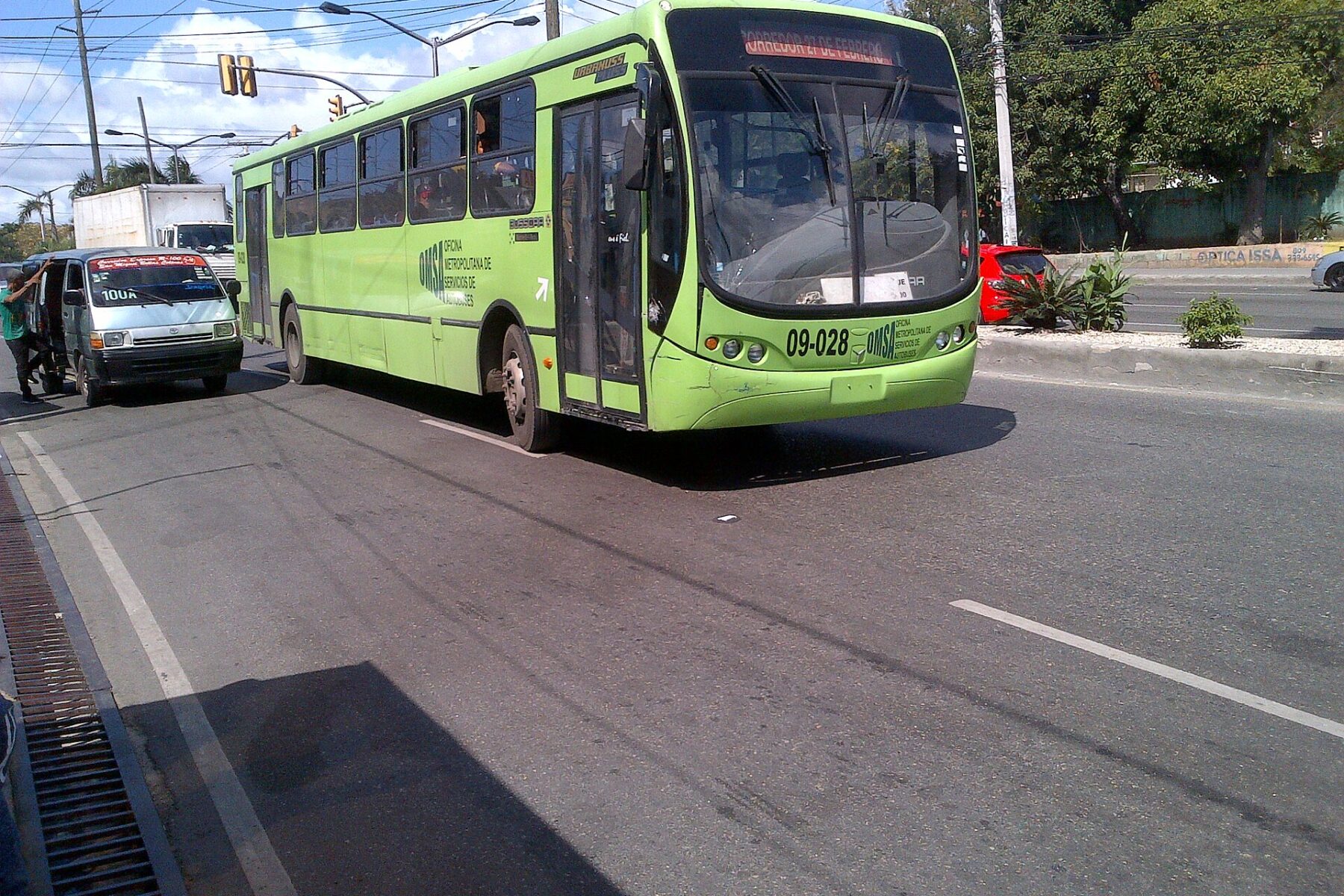 A green OMSA state bus on a main road in Santo Domingo, Dominican Republic