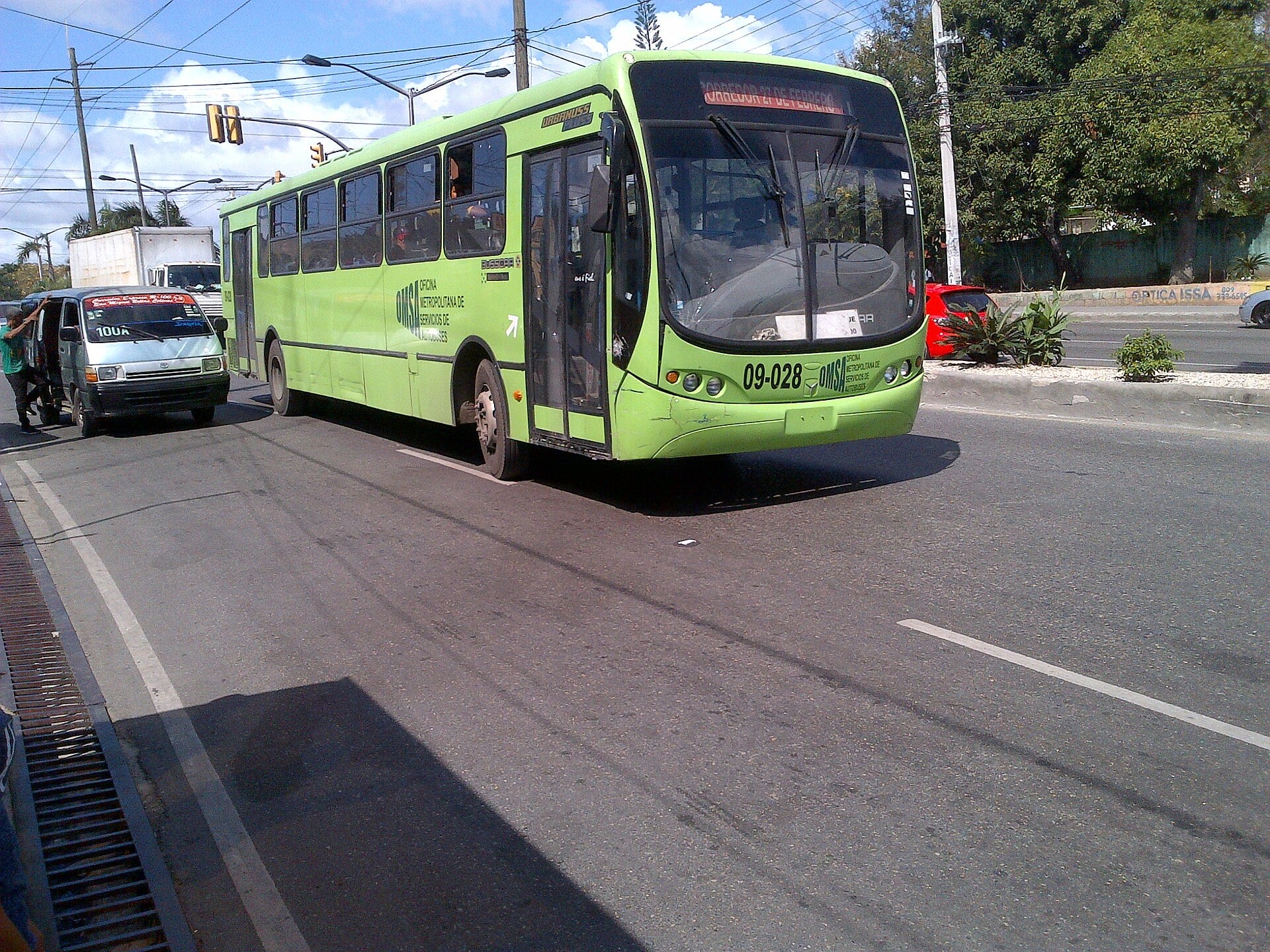 A green OMSA state bus on a main road in Santo Domingo, Dominican Republic