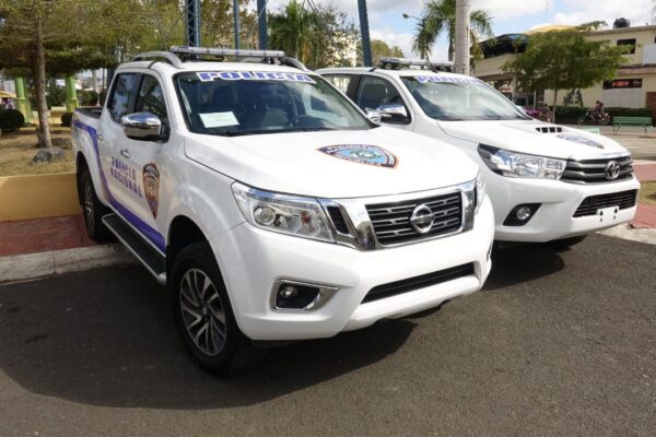 Dominican National Police pickup trucks parked in a town square, with the force's badge and the word Policía on the doors and windscreens.