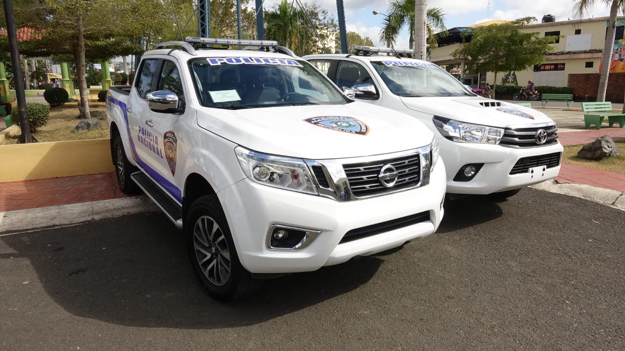 Dominican National Police pickup trucks parked in a town square, with the force's badge and the word Policía on the doors and windscreens.