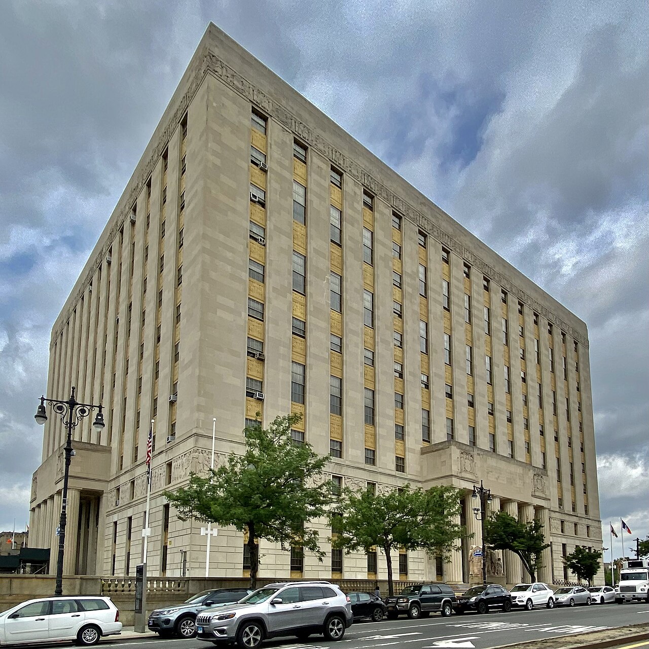 A large limestone courthouse with tall vertical windows and a columned entrance on a street in the Bronx under a cloudy sky