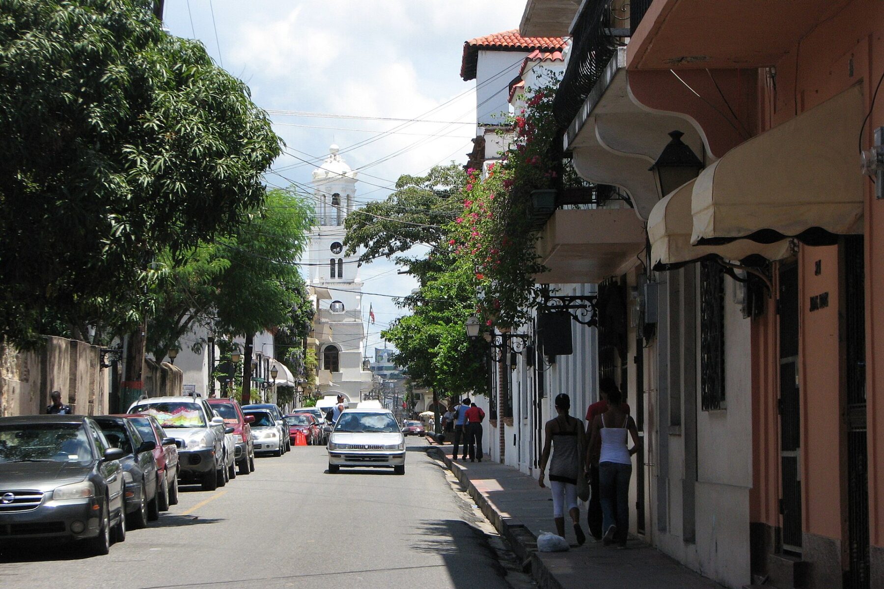 Street in the Colonial Zone of Santo Domingo, Dominican Republic, with parked cars and a white church tower