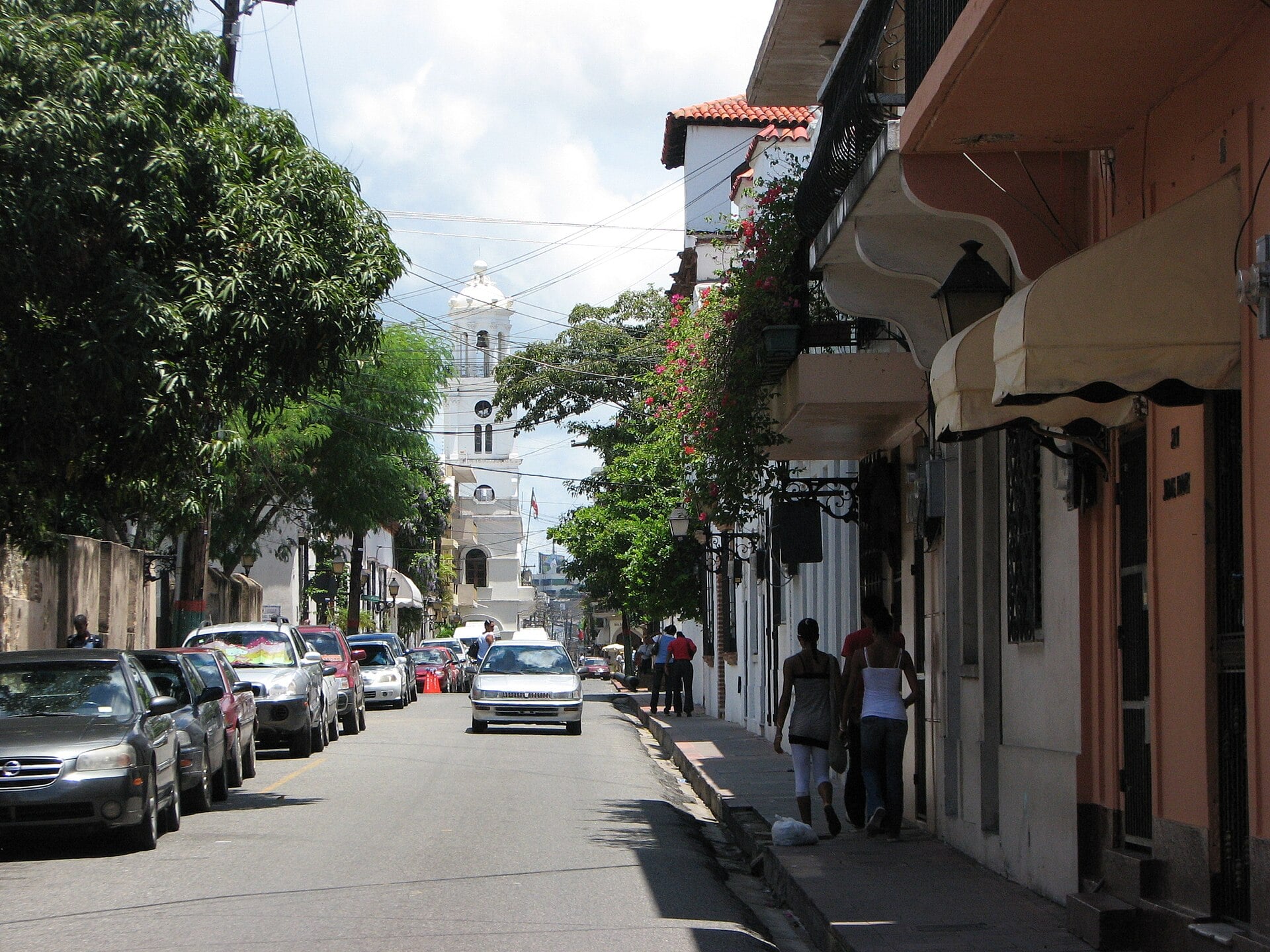Street in the Colonial Zone of Santo Domingo, Dominican Republic, with parked cars and a white church tower