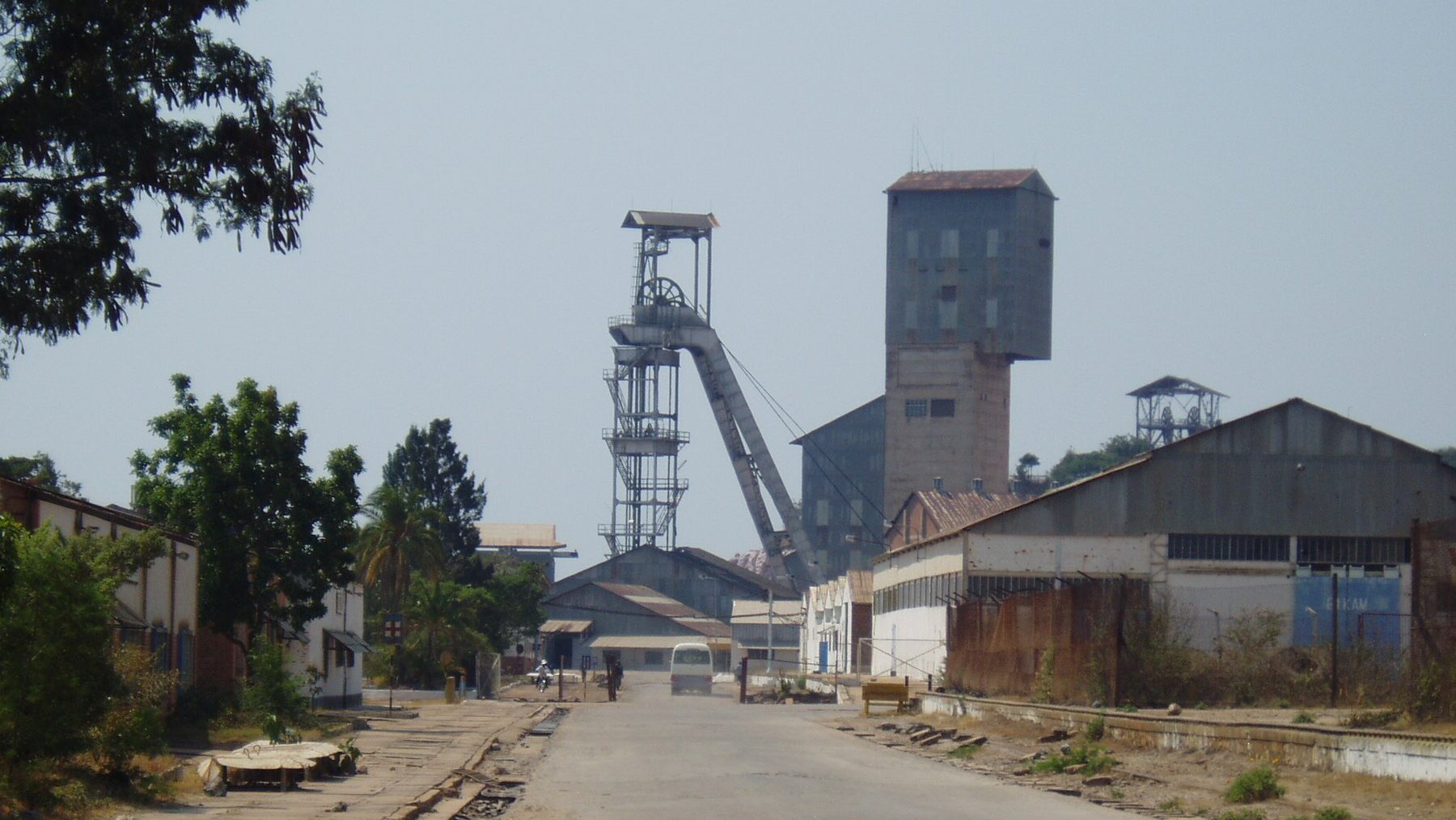 A steel mine headframe and a tall concrete shaft tower rise above sheds and a road at the Kamoto copper and cobalt mine near Kolwezi