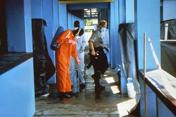 Health workers in orange protective suits and masks disinfect a blue-walled clinic corridor with a sprayer