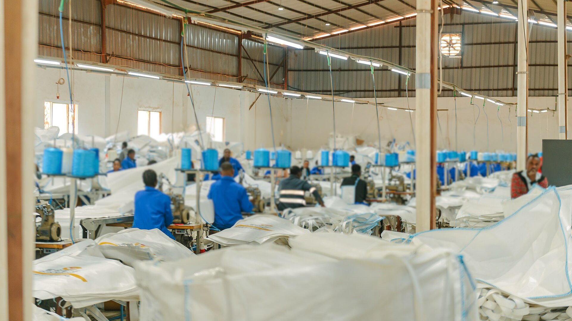 Workers in blue overalls sew large industrial bags at a bag and sack factory in Lubumbashi, DR Congo