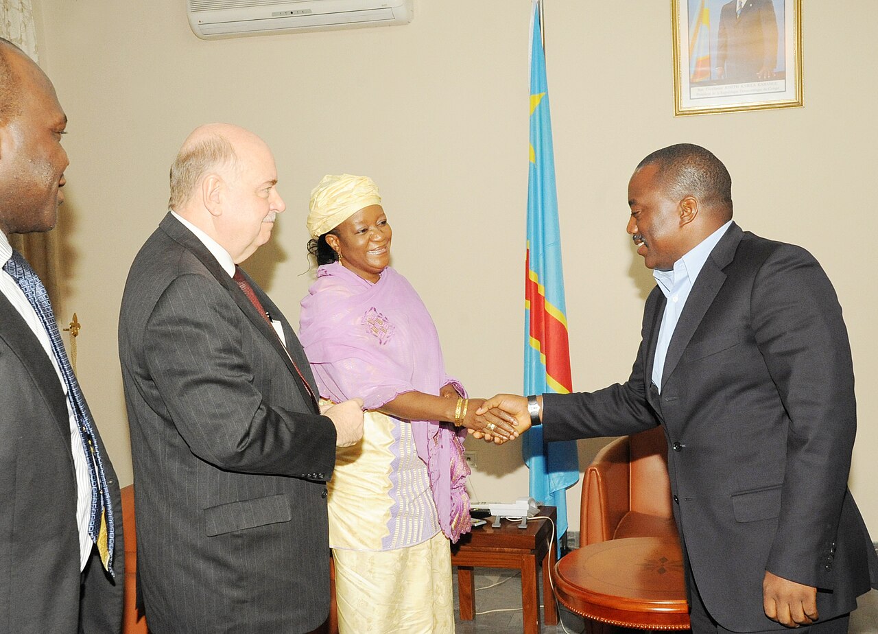 Joseph Kabila shakes hands with a UN envoy in an office beside a Congolese flag