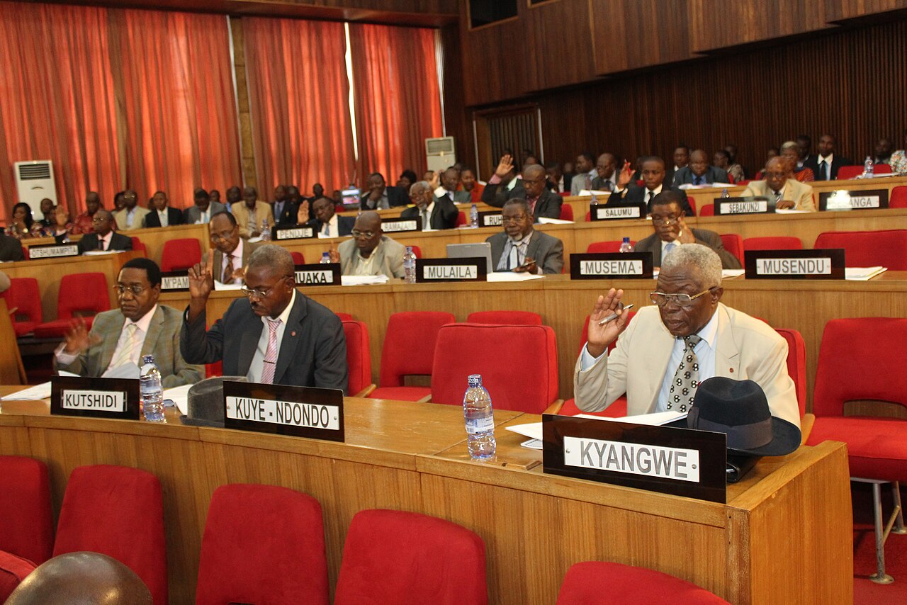 Congolese senators raise their hands to vote at their desks in the Senate chamber