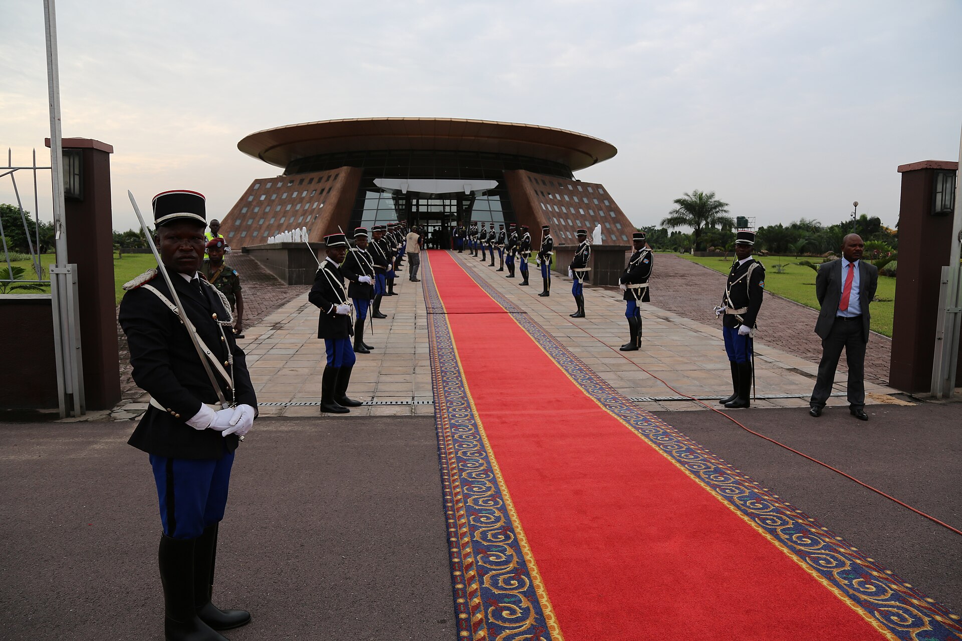 Ceremonial guards in dark uniforms line a red carpet outside a terminal building at N'djili airport in Kinshasa
