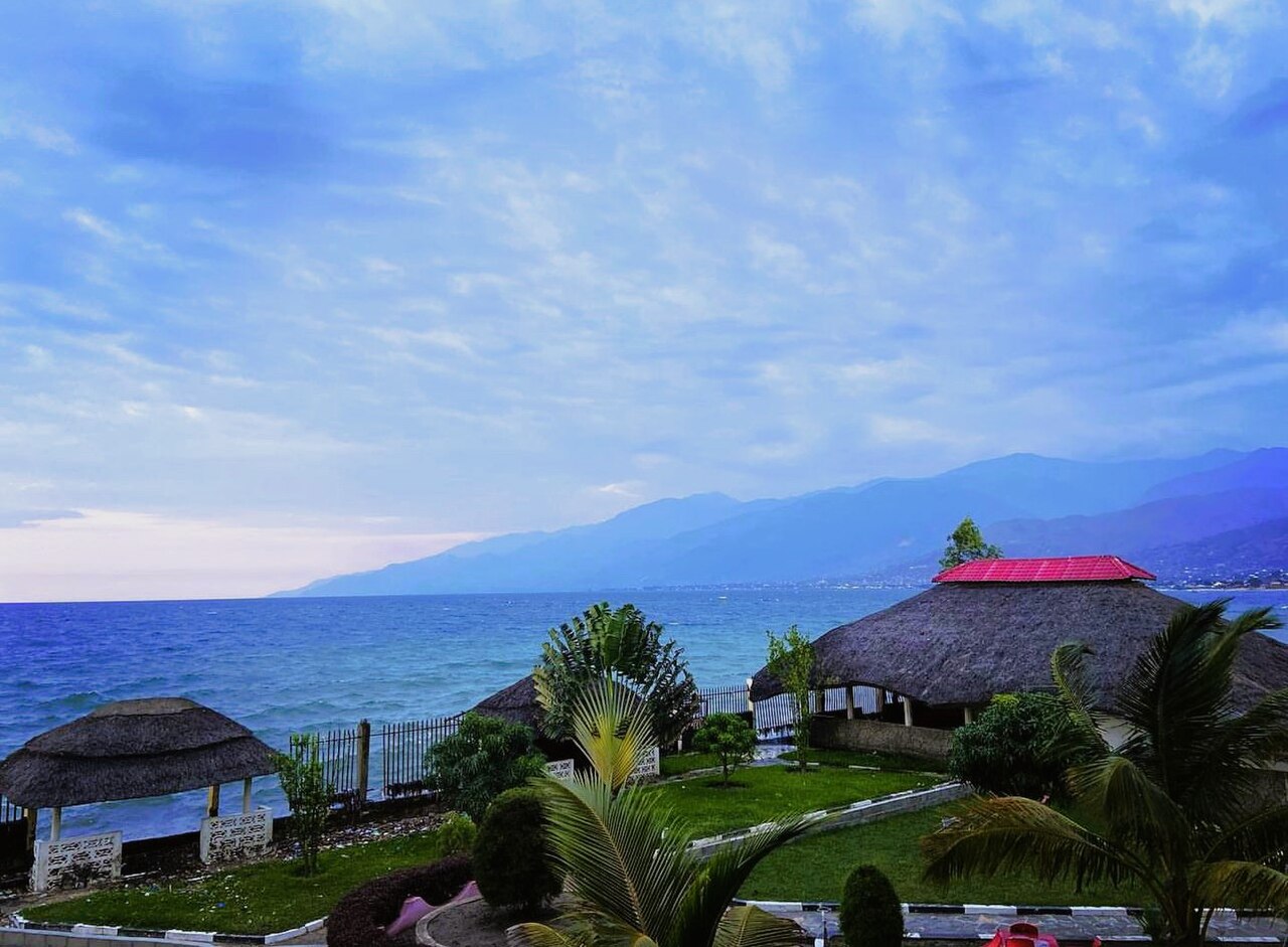 Thatched lakeside pavilions on the Lake Tanganyika shore at Uvira with blue mountains across the water