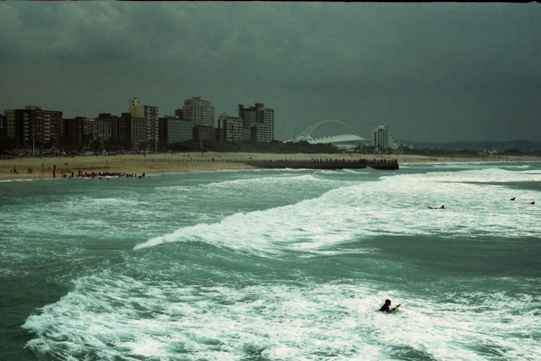 Durban beachfront in South Africa with apartment towers and the arch of Moses Mabhida Stadium under a stormy sky