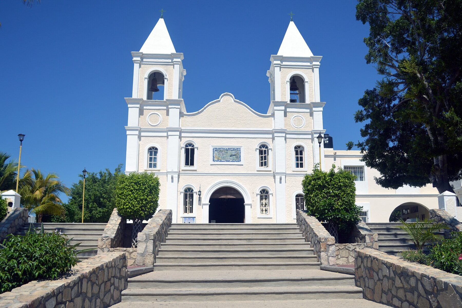 White mission church with two bell towers at the top of a wide stone staircase in San José del Cabo, under a clear blue sky
