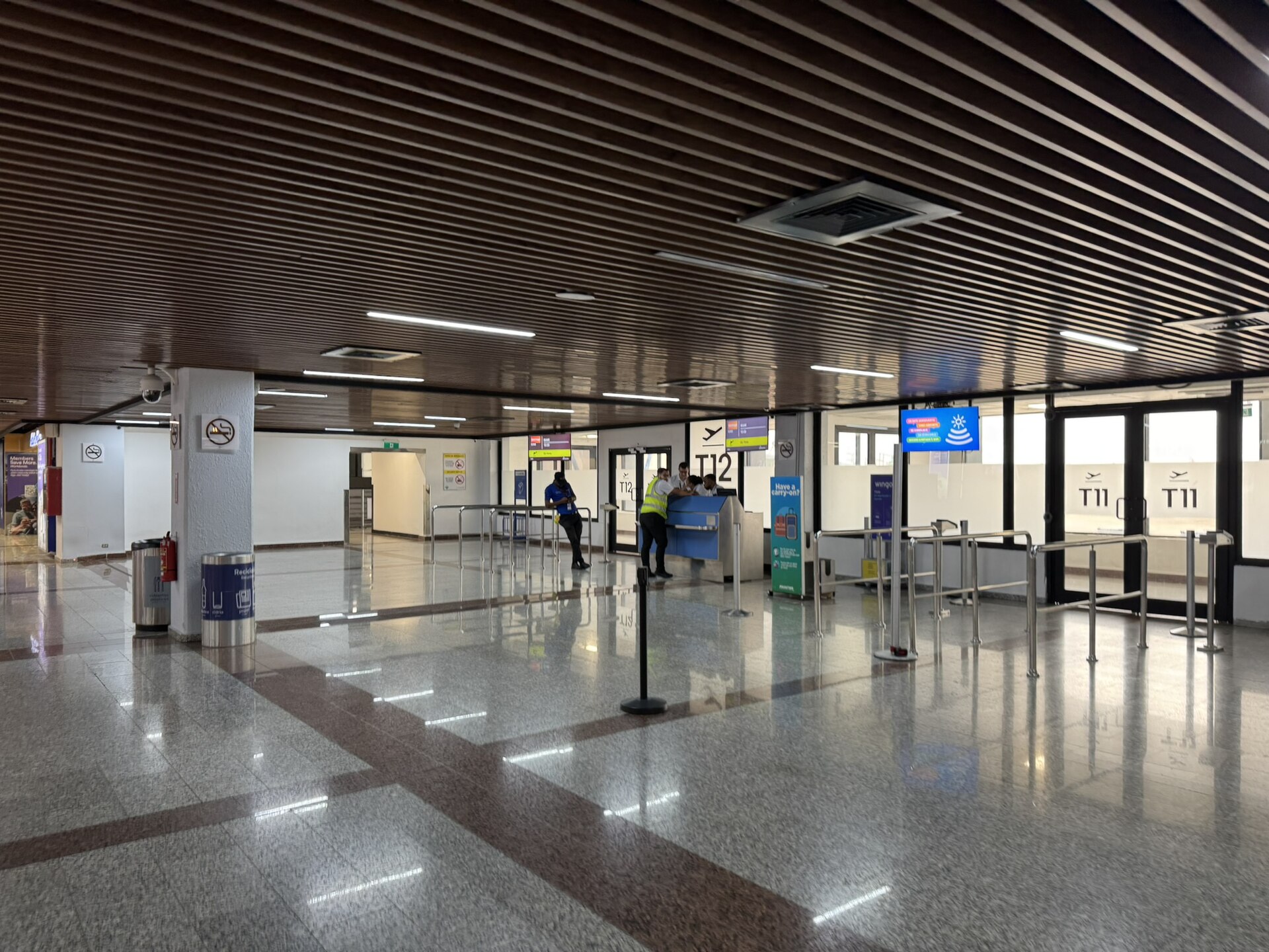 Departure gate area T11 and T12 with a check desk, queue barriers and staff inside Las Américas International Airport