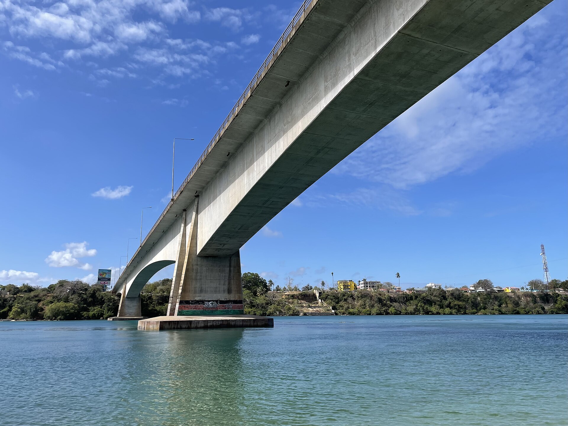 Concrete road bridge spanning the turquoise water of Kilifi Creek, with trees and buildings on the far bank