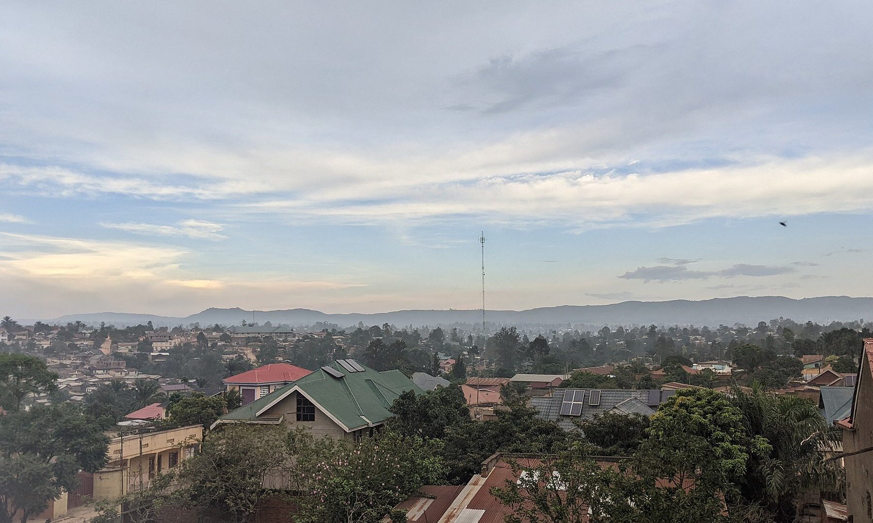 Rooftops of Bunia in Ituri province, northeast Congo, with a tall mast and hills under a dawn sky