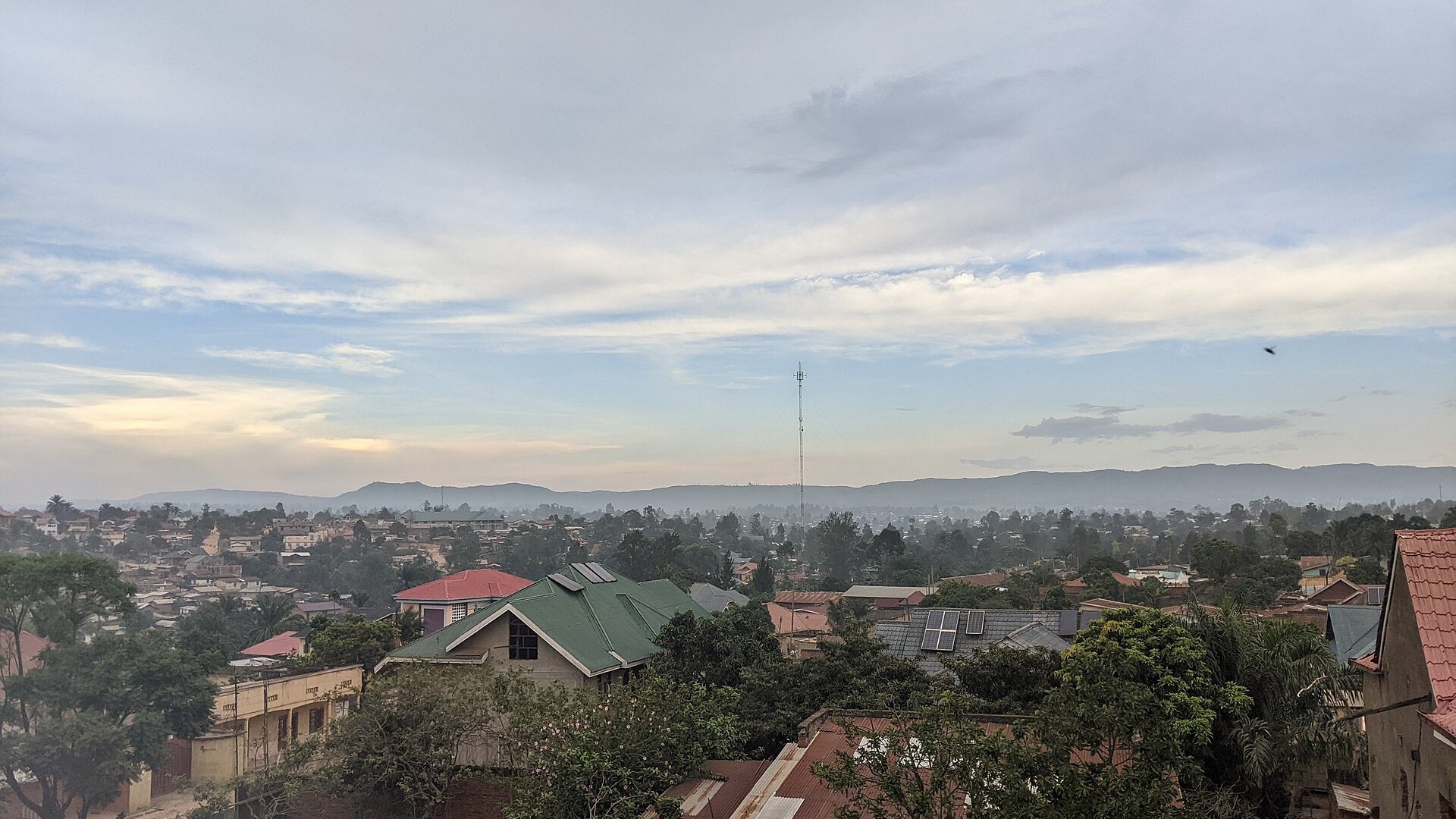 Rooftops of Bunia in Ituri province, northeast Congo, with a tall mast and hills under a dawn sky