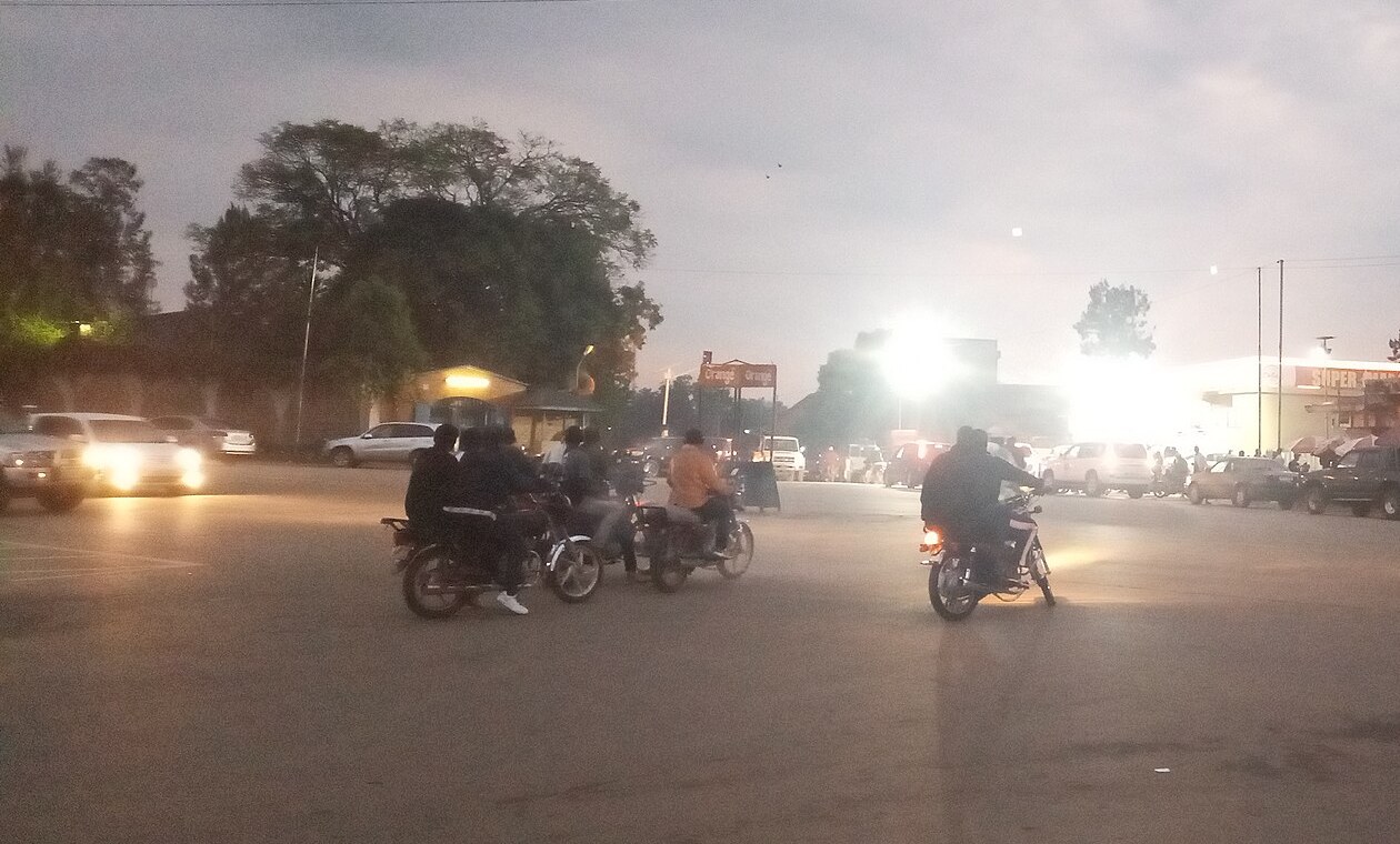 Motorbike taxis and cars at a roundabout in central Bunia at dusk