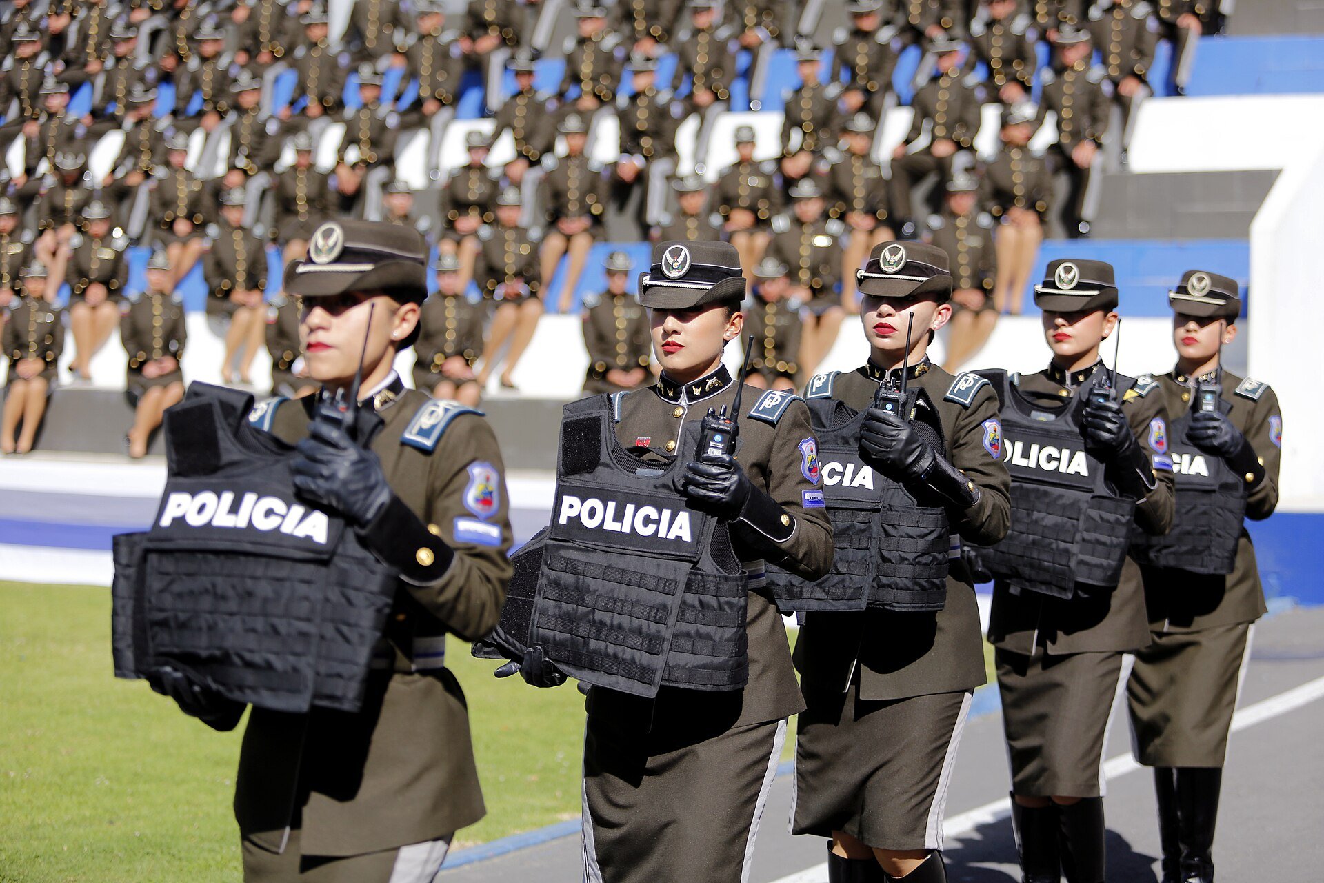 Ecuadorian National Police officers in dress uniform carry body armor marked Policia at a ceremony in Quito