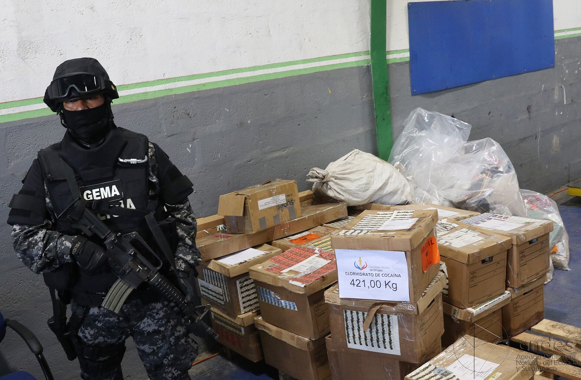 Armed Ecuadorian police officer stands beside boxes of seized cocaine labeled 421 kilograms before destruction in Quito