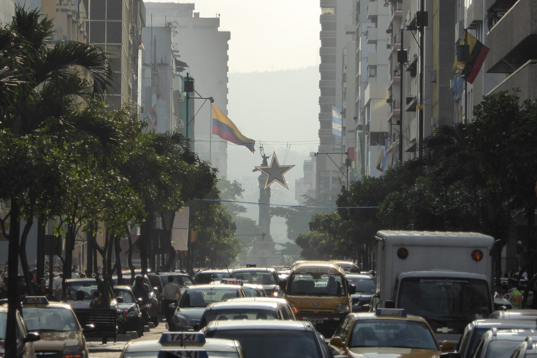 Taxis and traffic on Avenida 9 de Octubre in downtown Guayaquil with Ecuadorian flags and a column monument