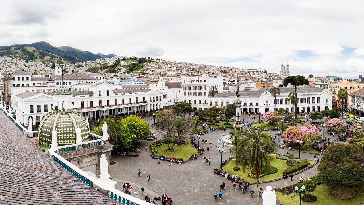 Aerial view of Plaza Grande, the main square of Quito, Ecuador, with white colonial buildings and people on the square below green hills