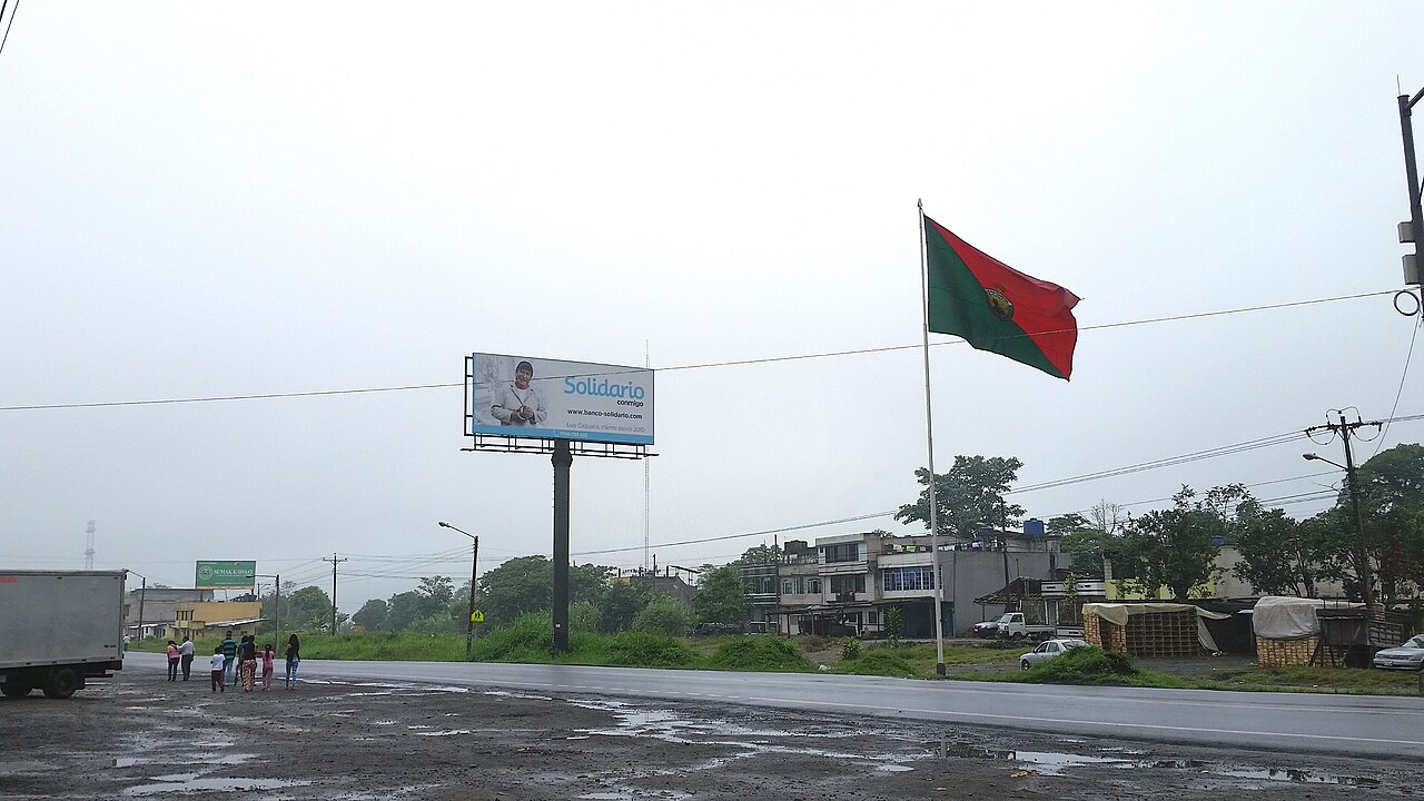 The E20 highway at the entrance to Santo Domingo, Ecuador, with a provincial flag and roadside buildings