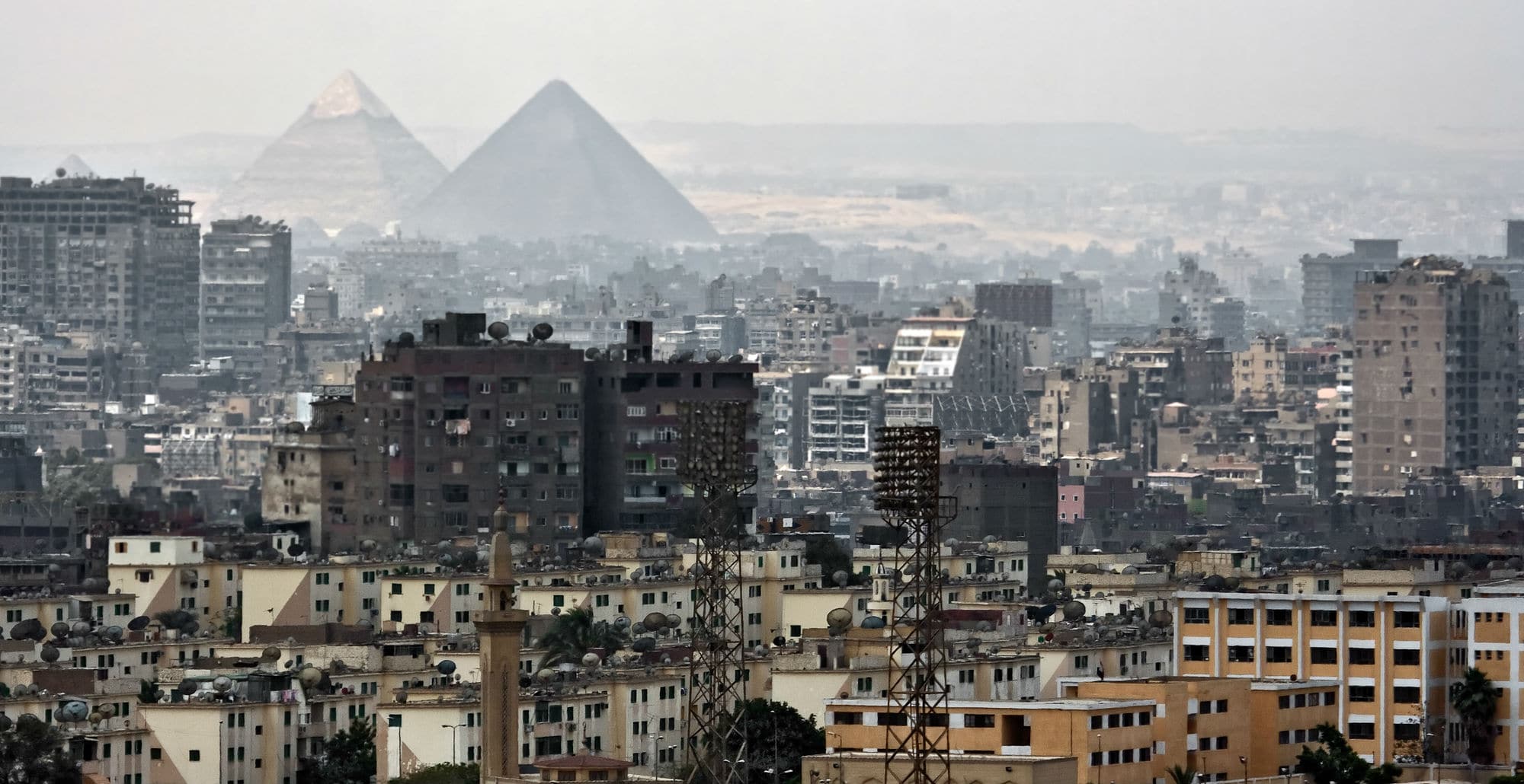 Apartment blocks across Cairo with the Giza pyramids rising in the haze behind them