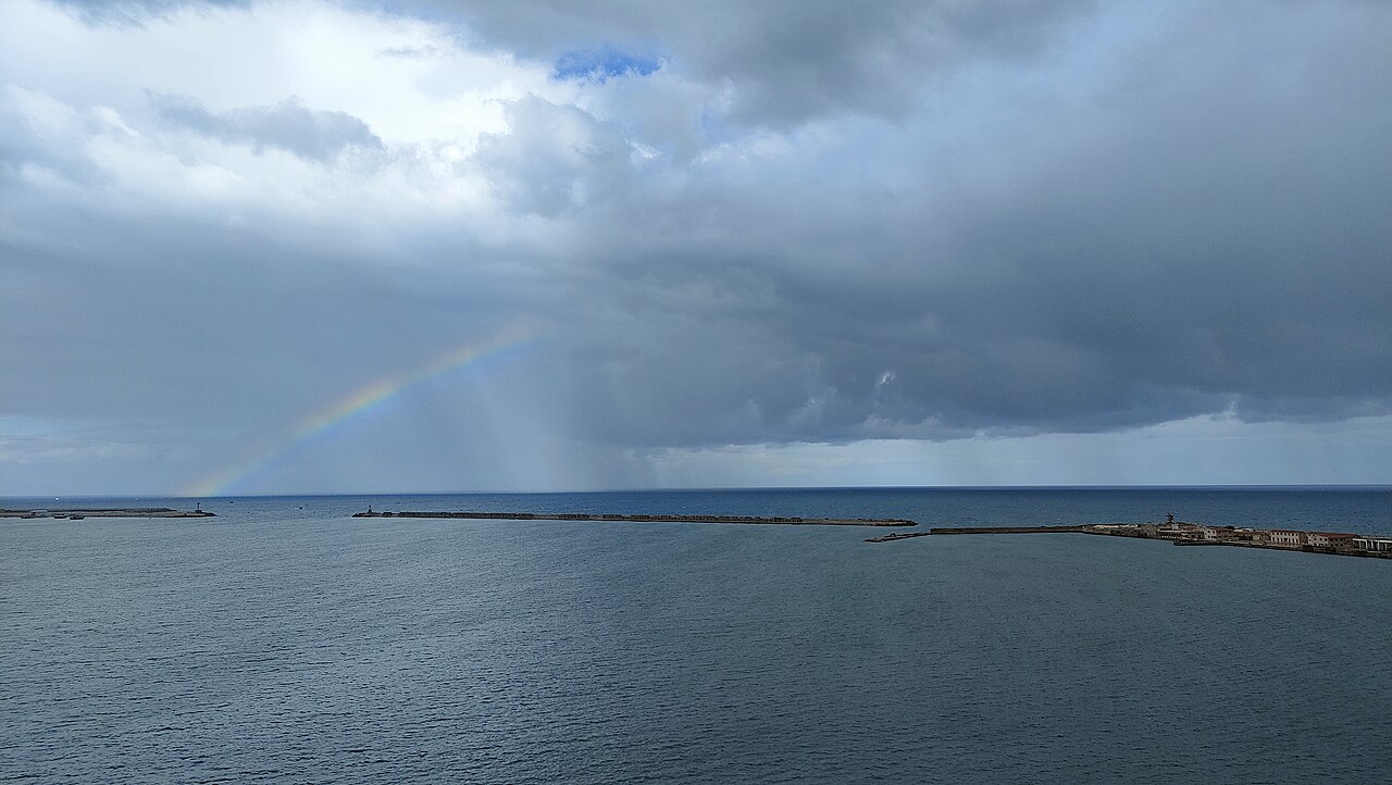 Breakwaters and a rainbow under storm clouds over the sea at the eastern harbour of Alexandria, Egypt