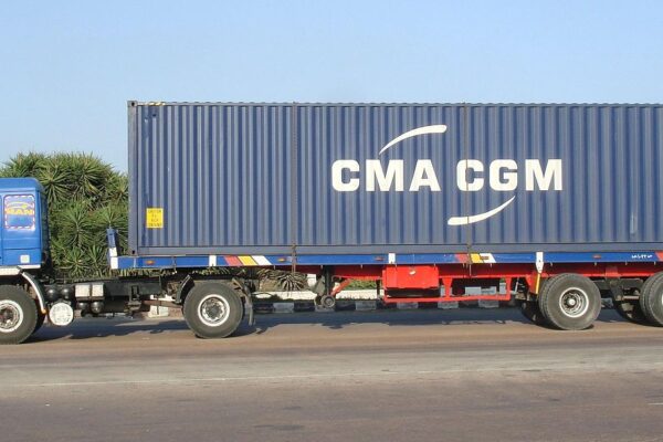 A blue truck carrying a CMA CGM shipping container along a road in Egypt