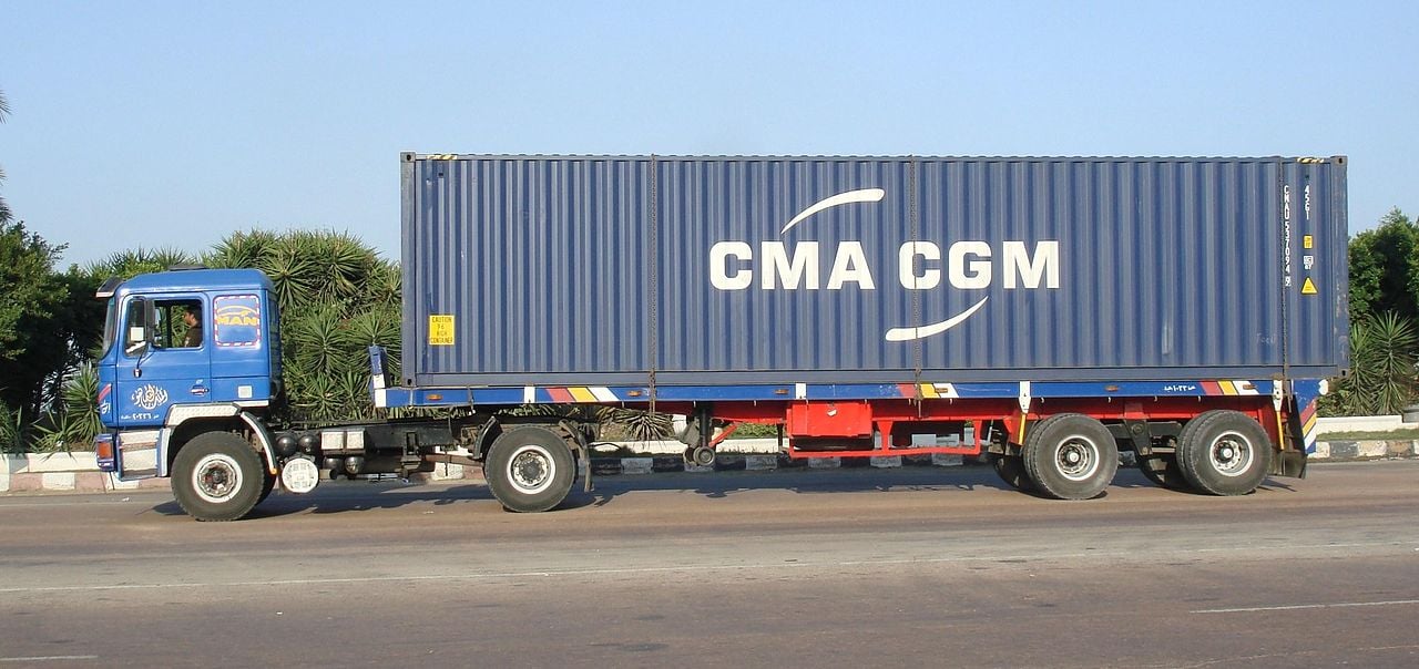 A blue truck carrying a CMA CGM shipping container along a road in Egypt