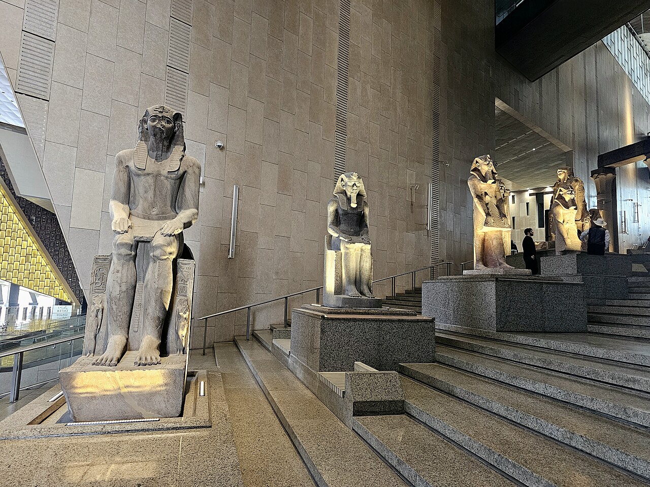 Seated pharaoh statues on granite plinths along the Grand Staircase inside the Grand Egyptian Museum