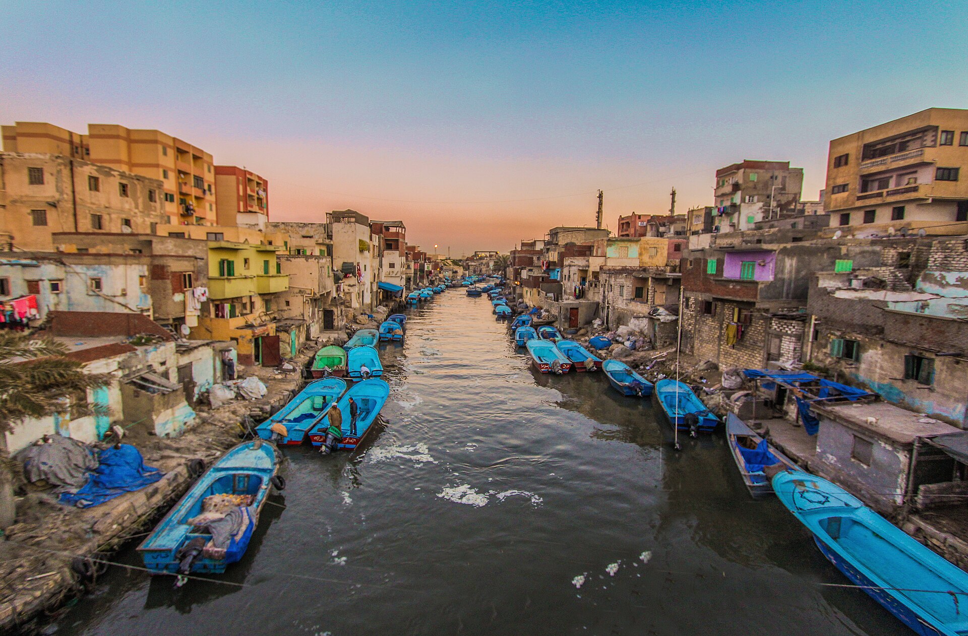 Blue fishing boats moored along a canal lined with houses in El Max, Alexandria, Egypt