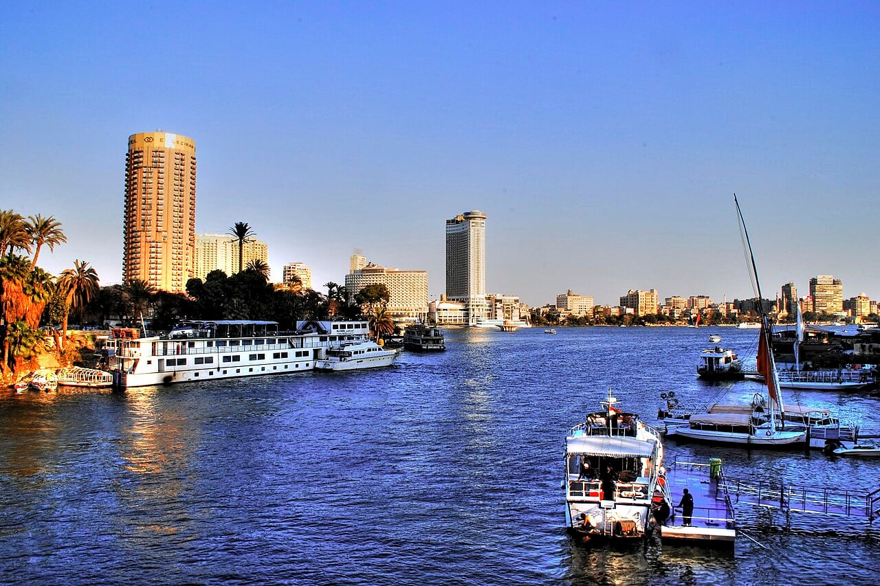 The Nile in Cairo with tourist boats, a felucca and hotel towers on the waterfront at sunset