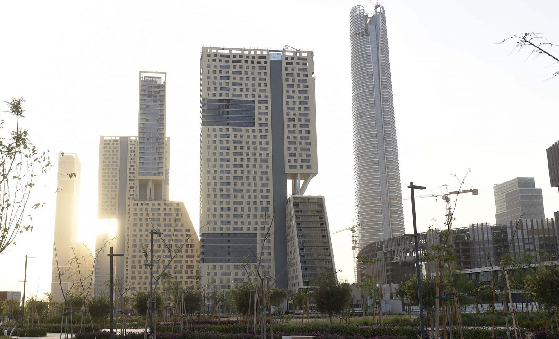 High-rise towers and a tall cylindrical skyscraper in the business district of Egypt's New Administrative Capital, with young trees in the foreground