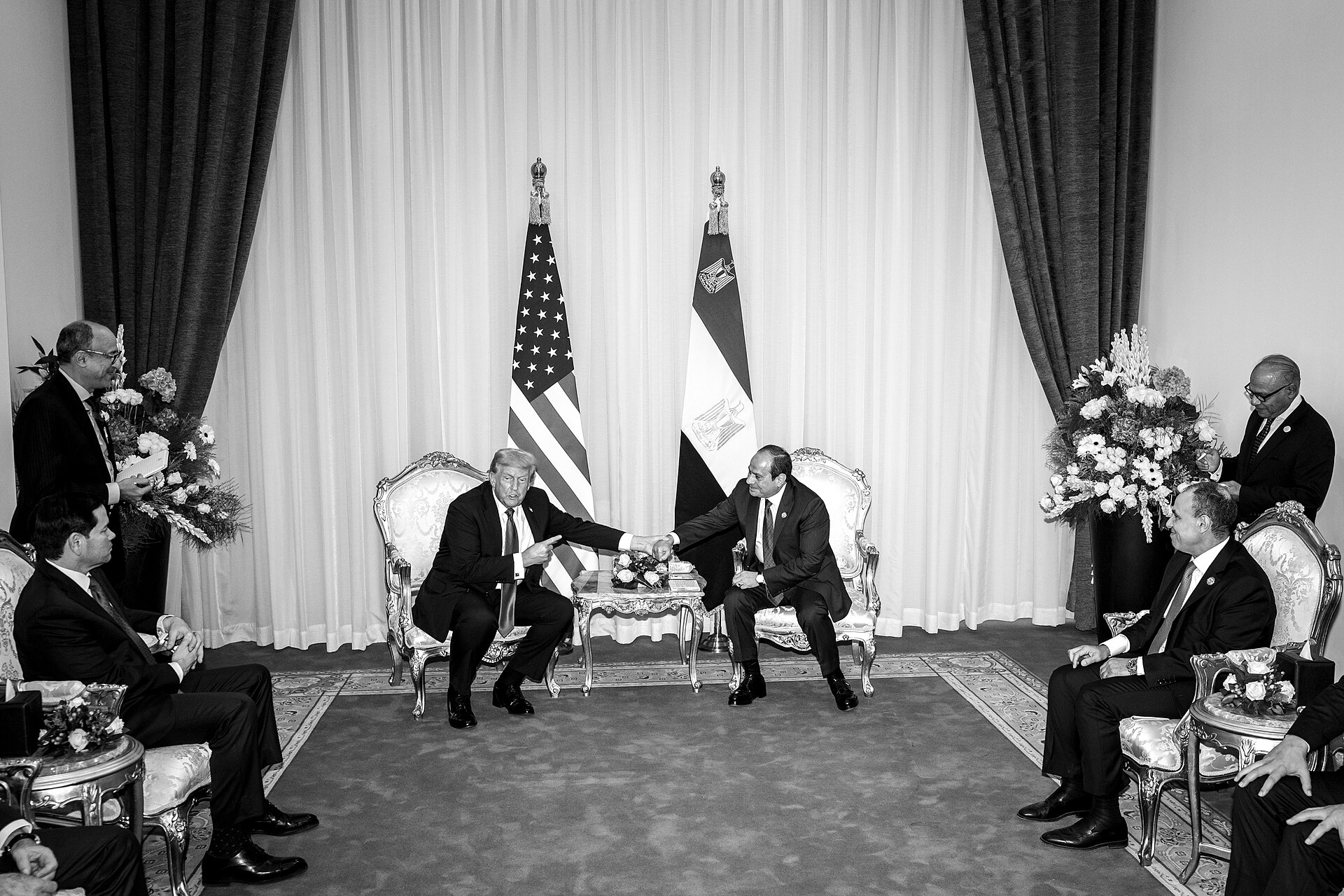 Donald Trump and Abdel Fattah el-Sisi seated in armchairs between the US and Egyptian flags, with officials from both delegations on either side