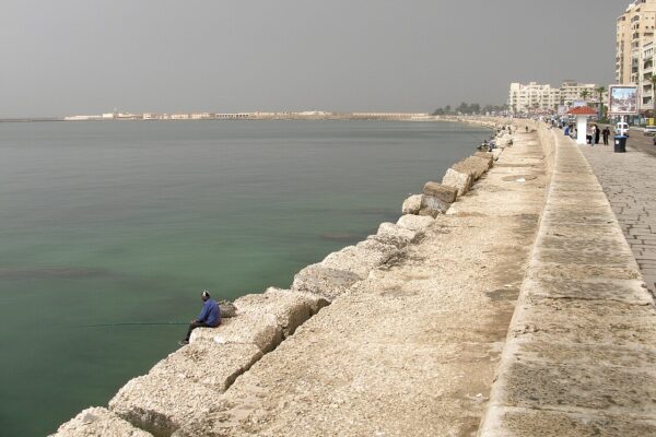 A fisherman sits on the stone seawall of the Alexandria Corniche on the Mediterranean coast of Egypt