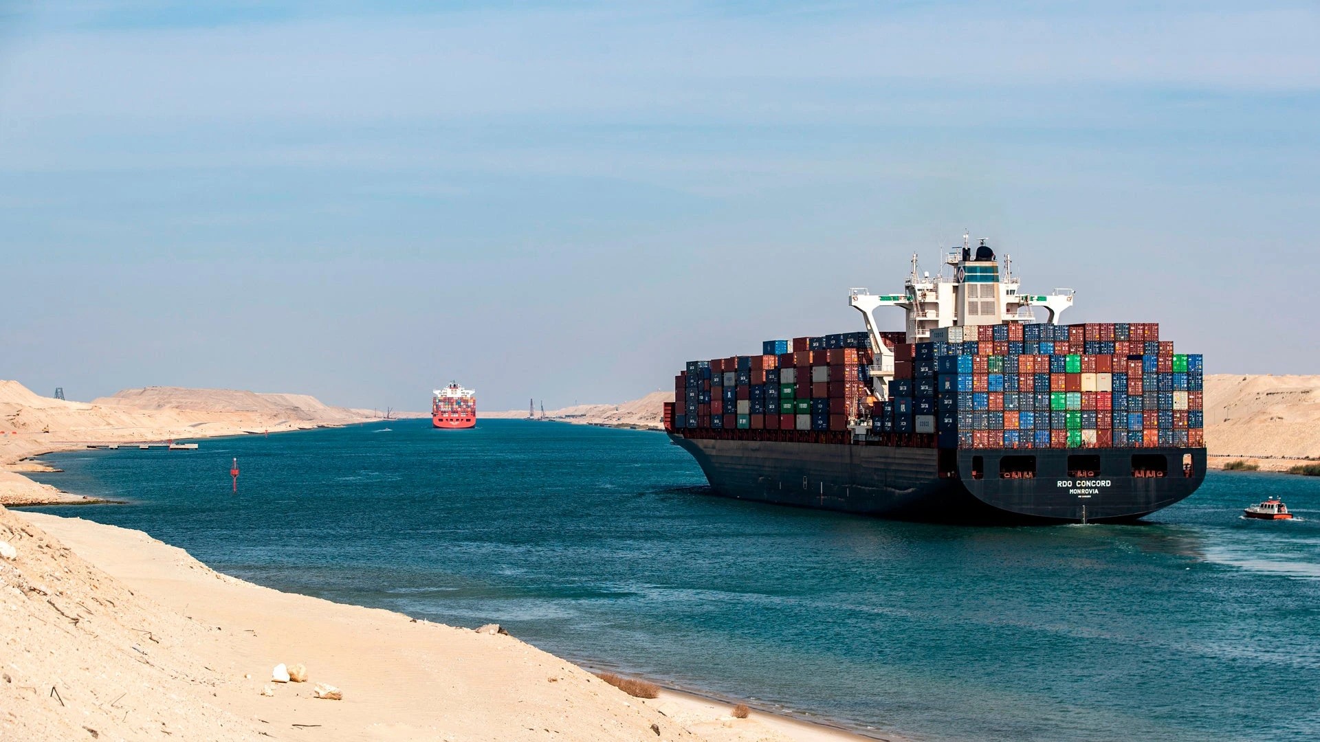 A loaded container ship passing through the Suez Canal between sandy banks in Egypt