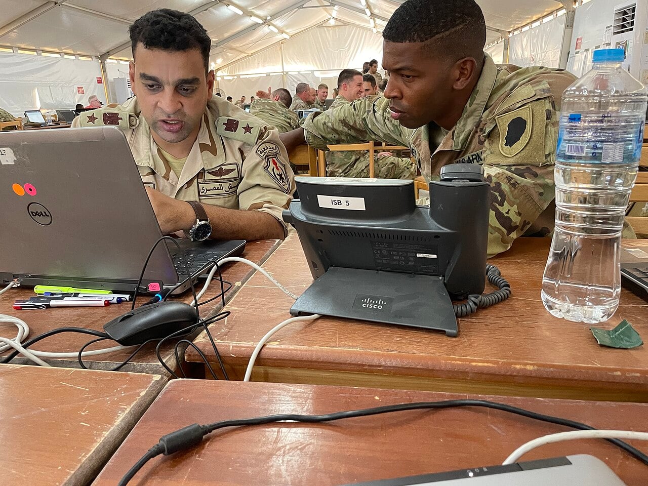 An Egyptian army officer and a US Army soldier work together at a laptop inside a large tent during the Bright Star 25 exercise in Egypt.