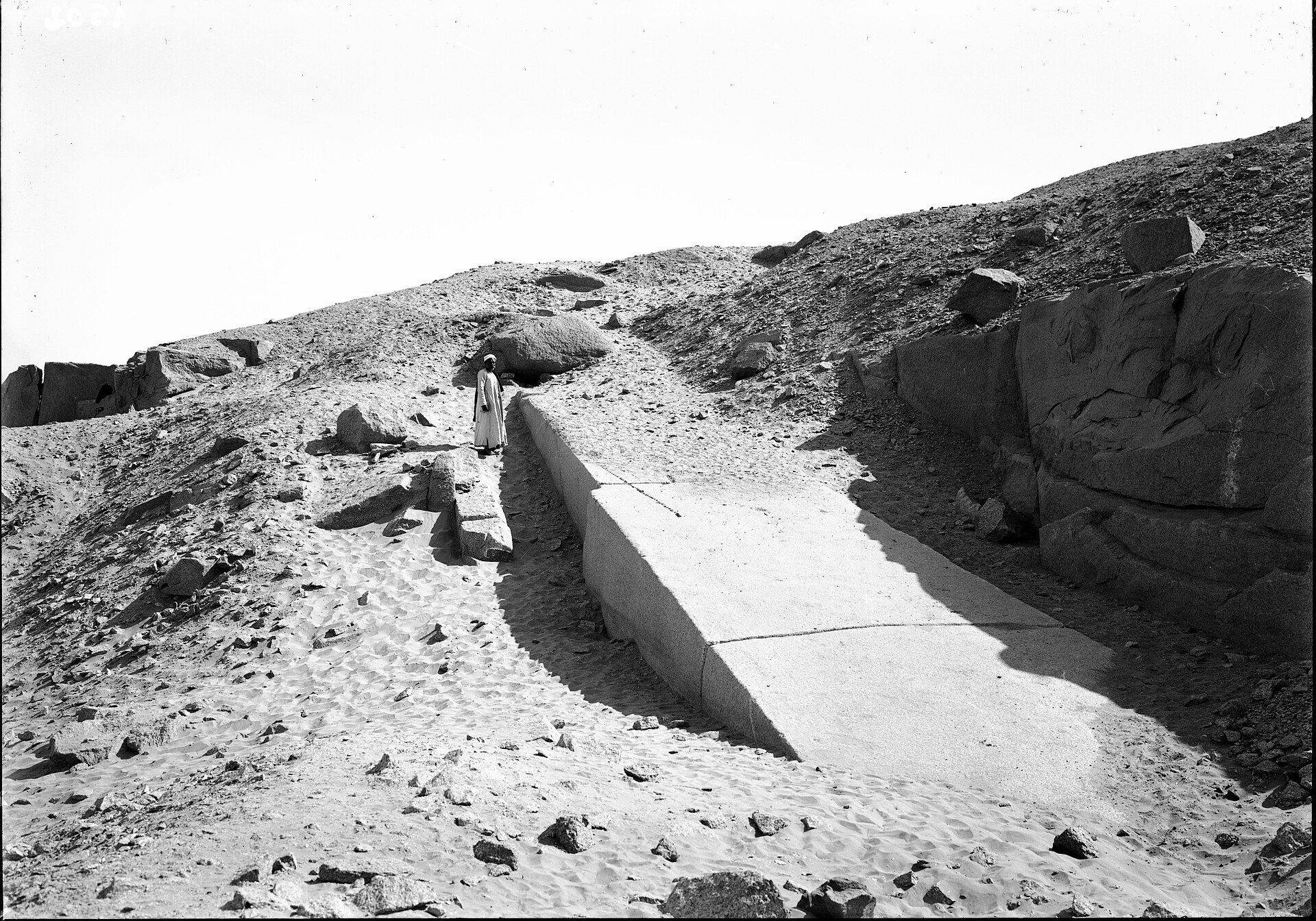 Granite quarry at Aswan in southern Egypt with a long cut stone slab on the ground and a man standing on the slope