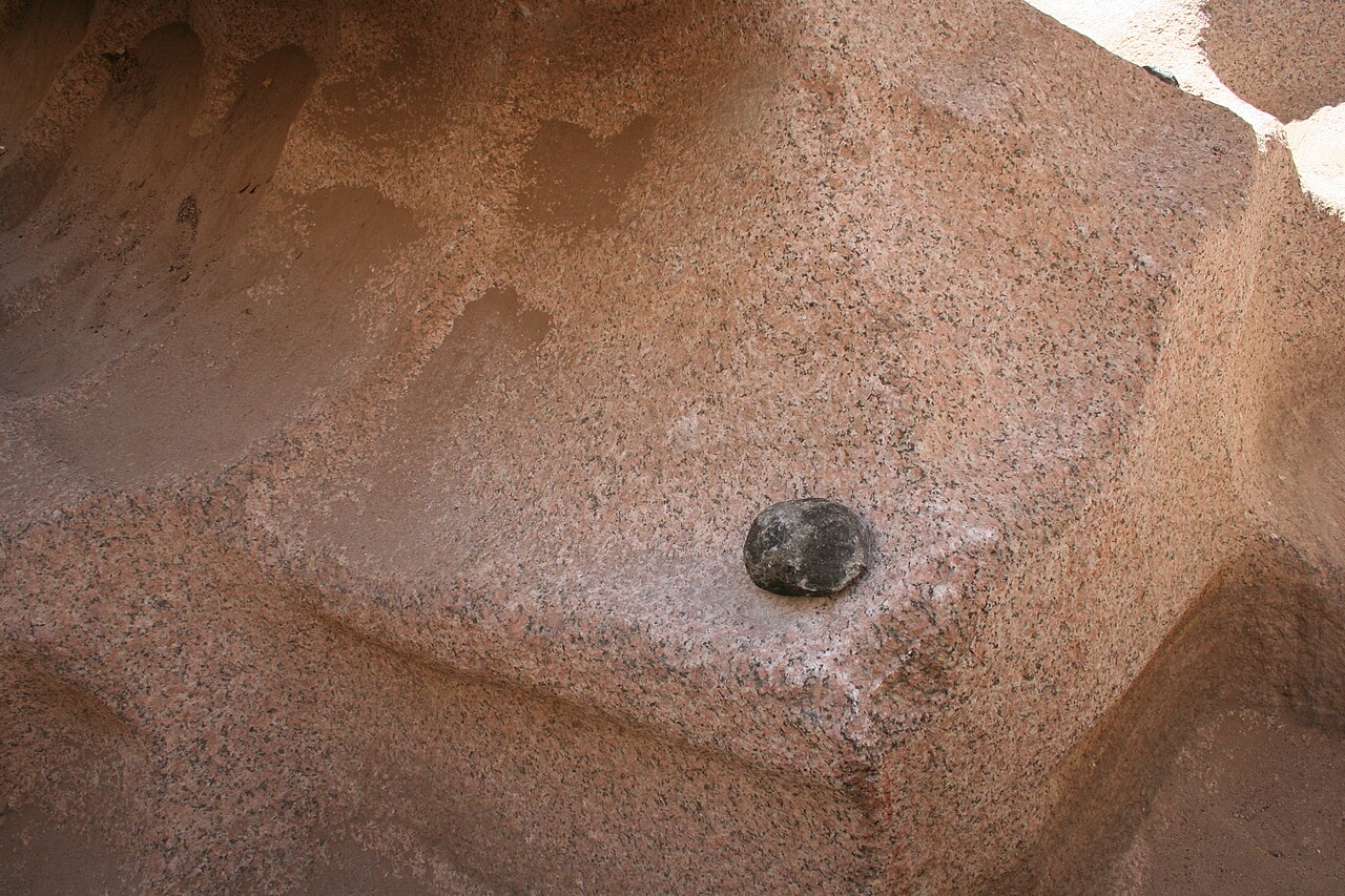 Pink granite wall at an Aswan quarry, cut into steps, with a dark dolerite pounding stone resting on the rock