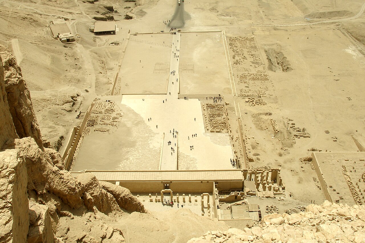 Aerial view from the cliff of the courts and terraces of the Temple of Hatshepsut at Deir el-Bahari, with visitors walking the central ramp.