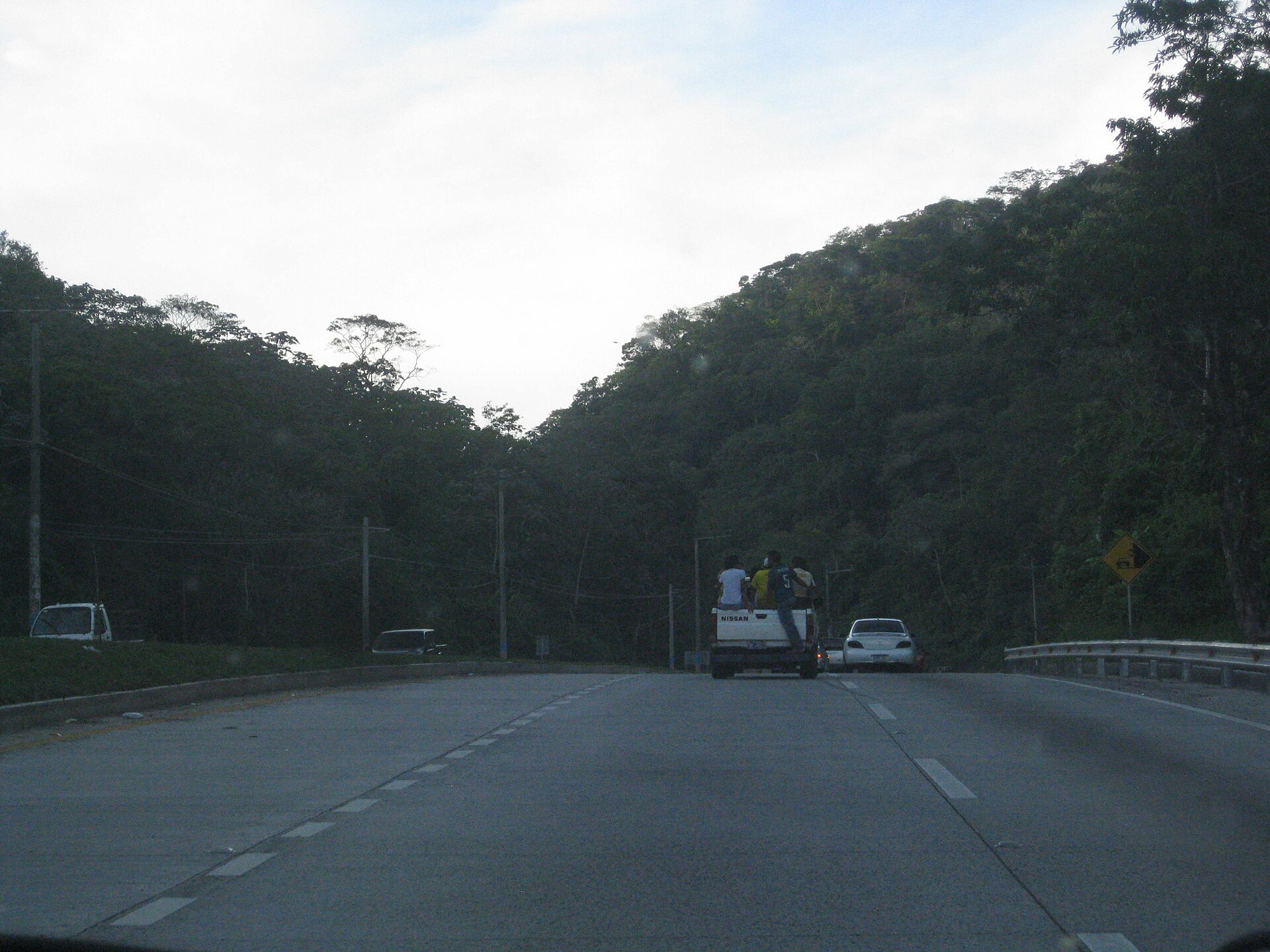 Traffic on the CA-4 highway in El Salvador, with passengers riding in the bed of a pickup truck