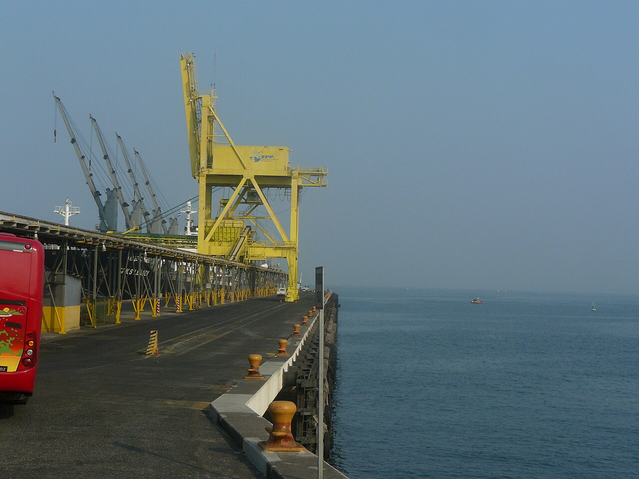 A yellow loading crane stands over a long concrete pier beside a docked cargo ship at the port of Acajutla, El Salvador