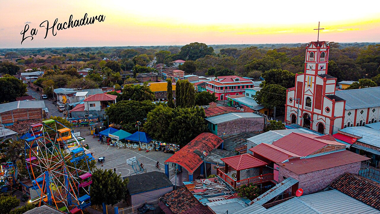 Aerial view at sunset of La Hachadura, a Salvadoran border town with a red and white church, rooftops and a small fairground