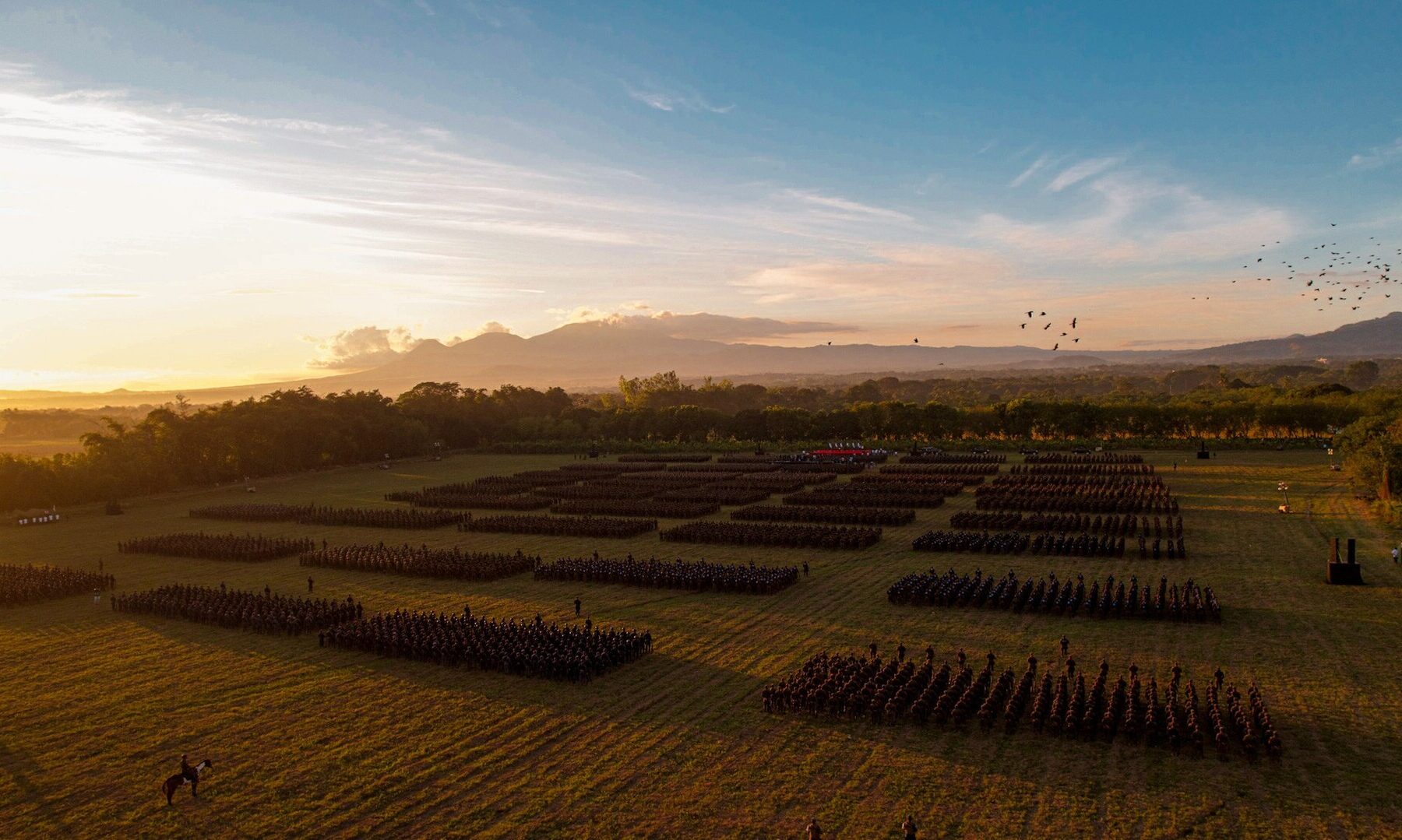 Aerial view of Salvadoran armed forces units in formation at sunset with a volcano in the background in El Salvador