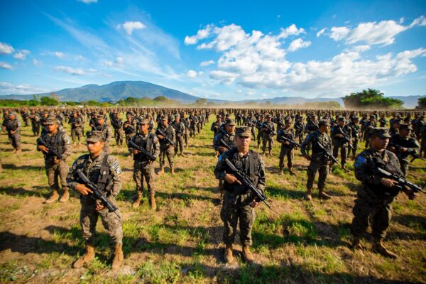 Latin America Defense Monitor cover: rows of Salvadoran soldiers in combat gear standing in formation in a field under a blue sky