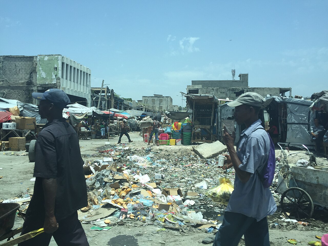 Pedestrians walk past a rubbish-strewn market area with damaged buildings in Port-au-Prince, Haiti