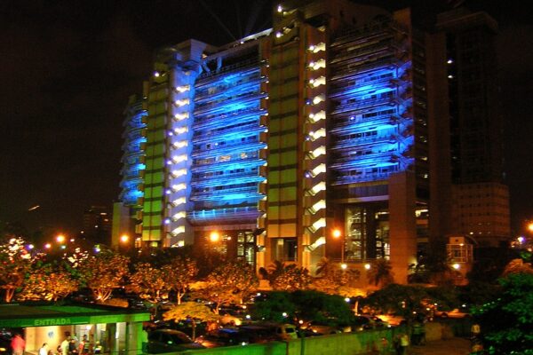 The blue-lit EPM headquarters tower in Medellín at night, with trees and street lights in front