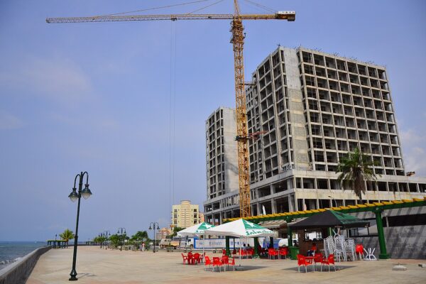 A tower block under construction beside the seafront promenade in Bata, Equatorial Guinea, with a tower crane and a cafe