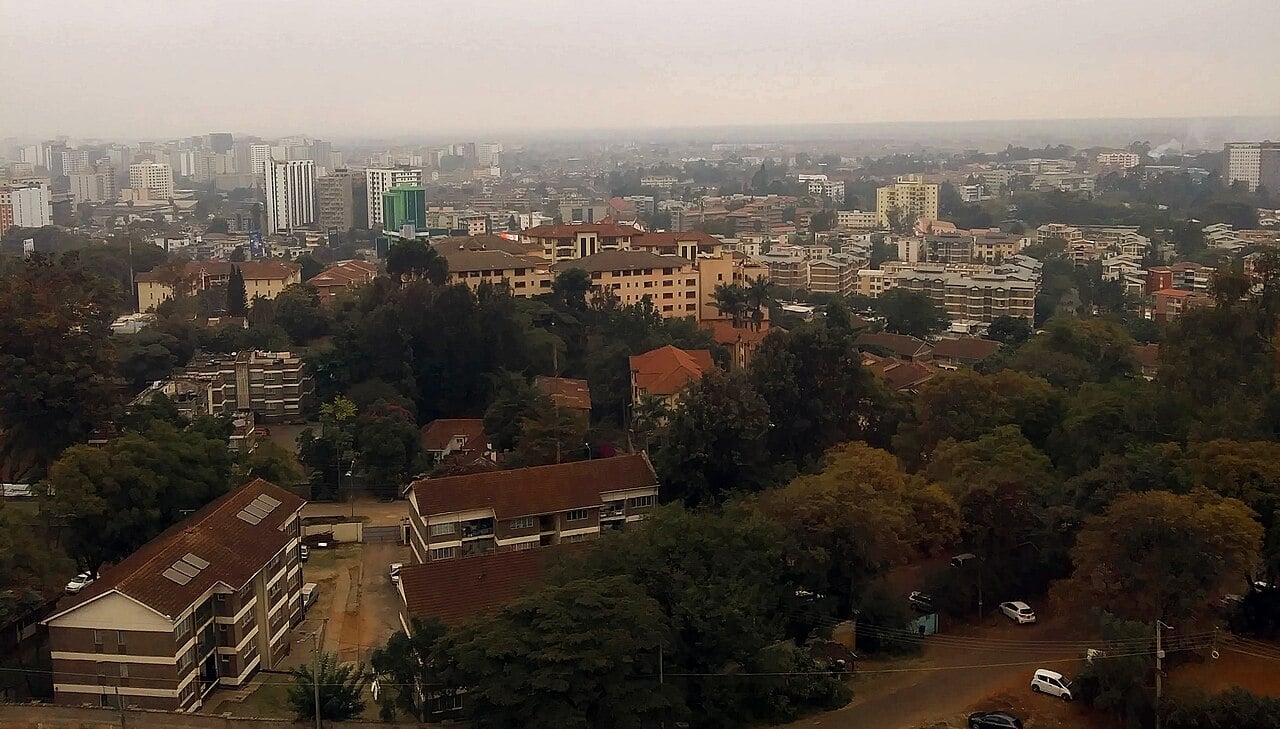 Apartment blocks and trees in Nairobi's Upper Hill district under a hazy sky, with high-rise buildings in the distance